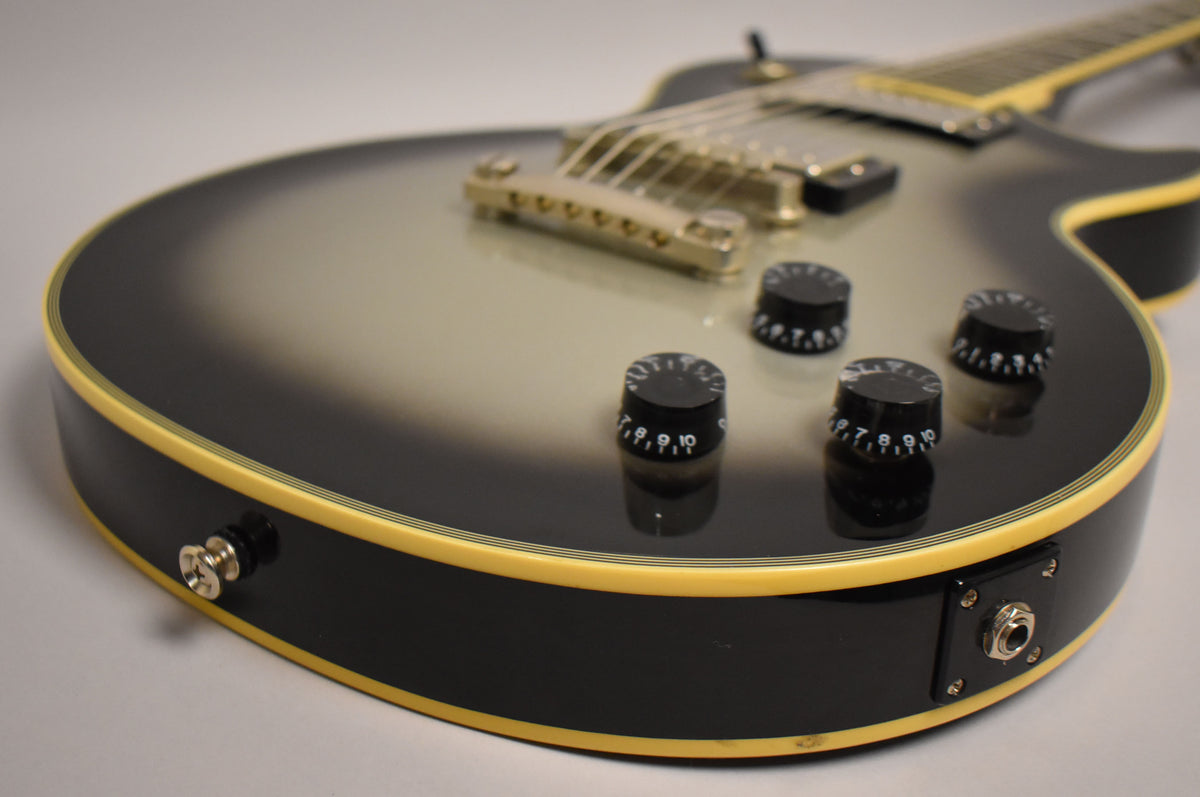 Close-up of the guitar's lower body, showing the silverburst finish, cream binding, four black control knobs, and output jack.