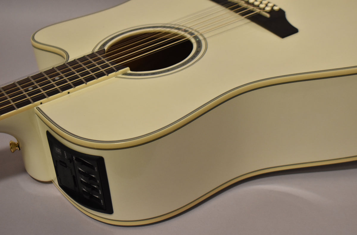 The pearl white 12-string dreadnought acoustic-electric guitar is angled to show its cutaway, soundhole, and black preamp controls on the side.