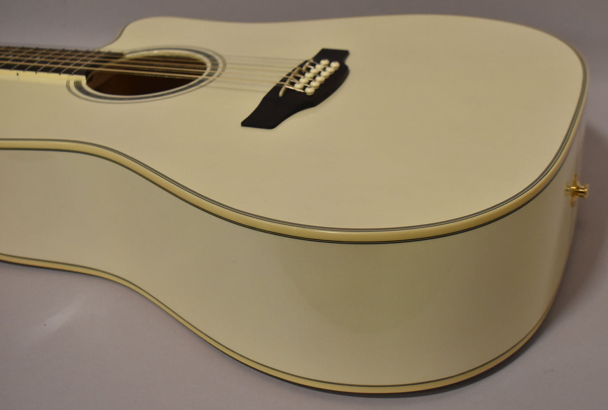 The pearl white dreadnought body is angled right, showing the cutaway, soundhole, black bridge with 12 pins, and a gold strap button.