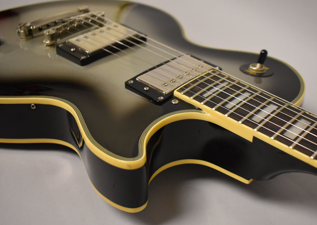 Close-up of a silverburst Les Paul body, showing the bridge, neck pickup, and lower fretboard with block inlays.