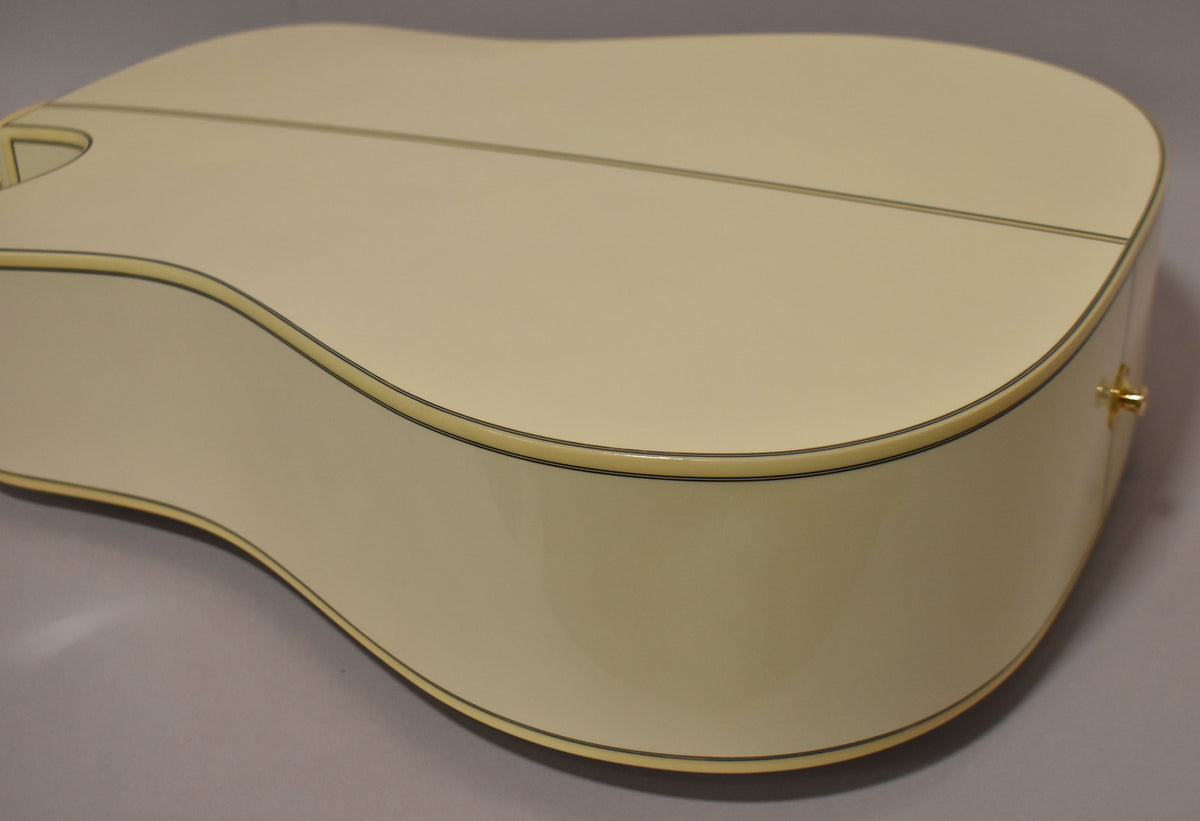 The lower bout of a pearl white acoustic guitar, showing the glossy back and side with cream binding and a gold strap button.