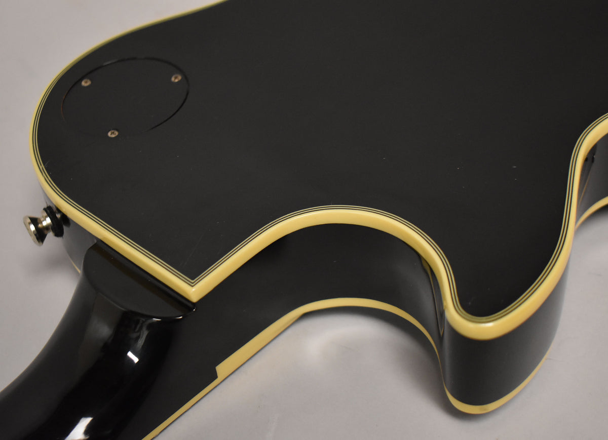 The guitar's black body, with cream binding and thin black stripes, shows light scratches and a circular control plate on the back.