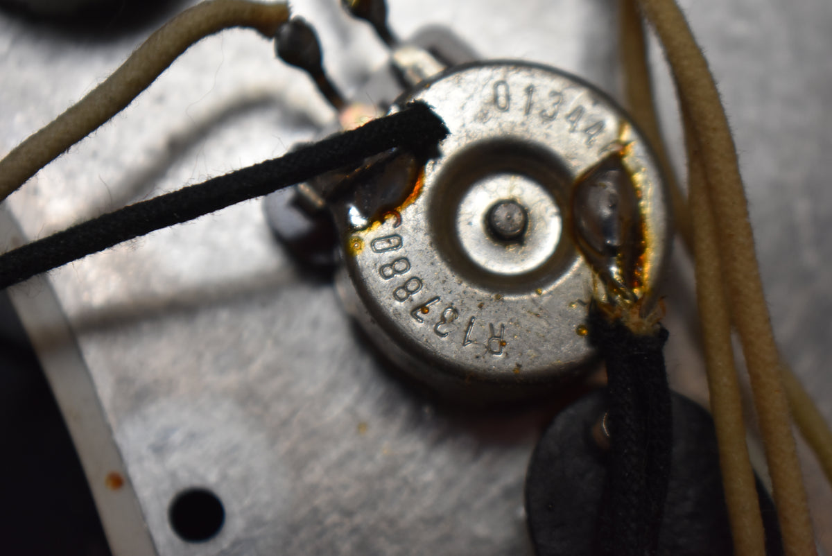 Close-up of a silver potentiometer with "R1378803" and "01344" stamped on it, connected by black and tan cloth-covered wires.