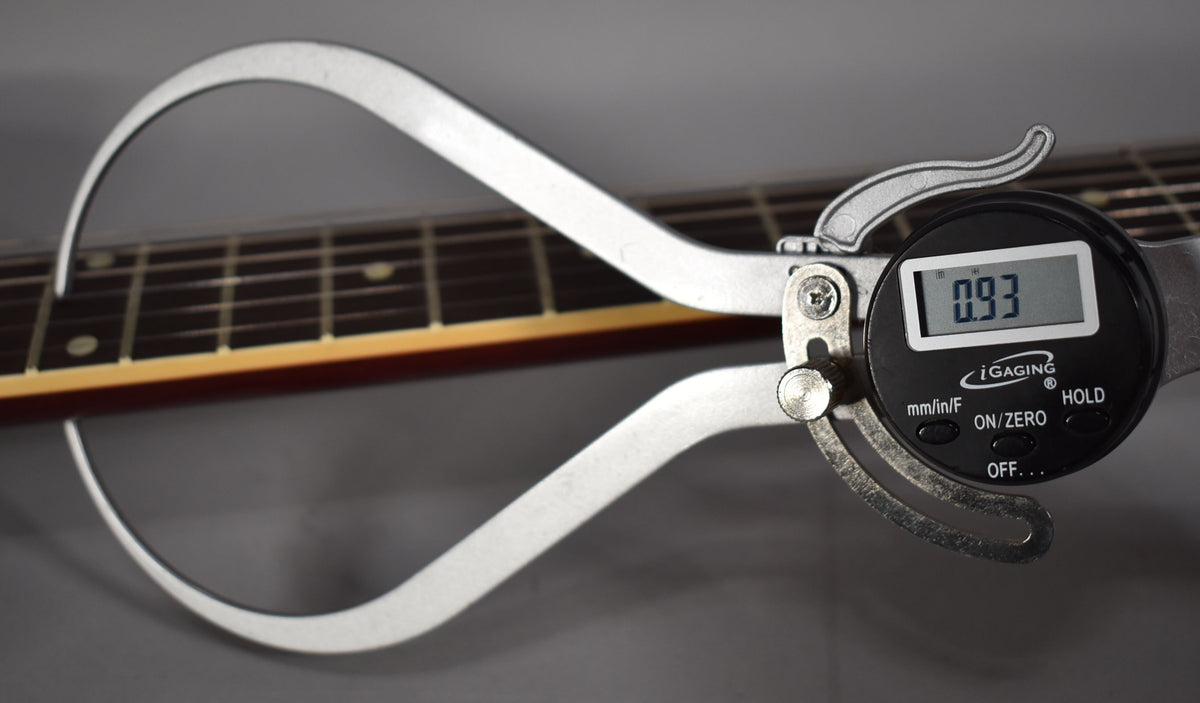 A digital caliper measures the guitar's neck thickness at 0.93 inches, showing the dark fretboard and cherry red neck binding.