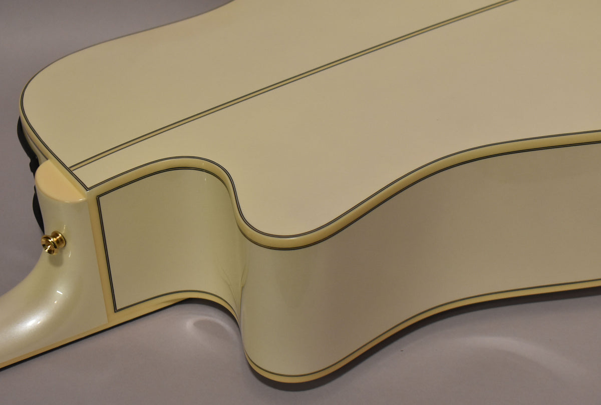 Close-up of the guitar's lower bout and cutaway, showing the pearl white finish, black binding, and a gold strap button on the heel.