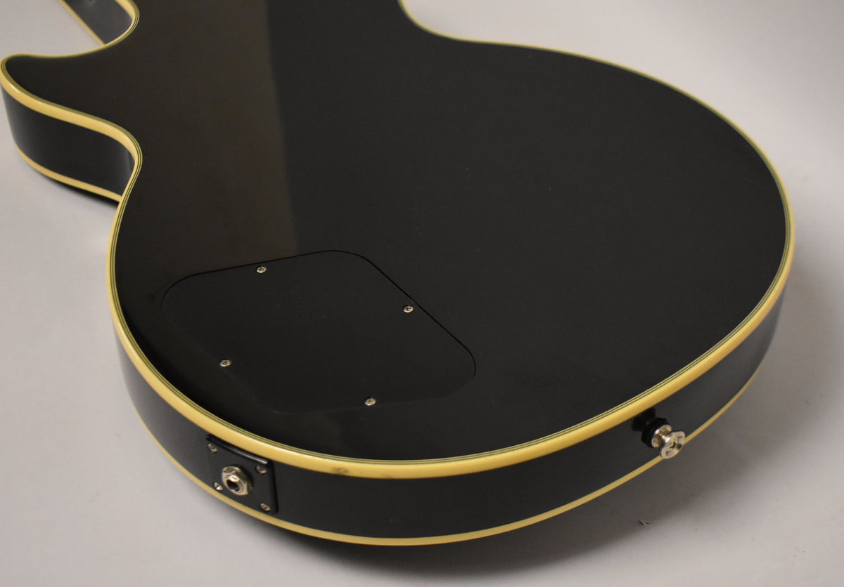 The guitar's black back and side are shown, with cream binding, a control cavity cover, and a chrome output jack.