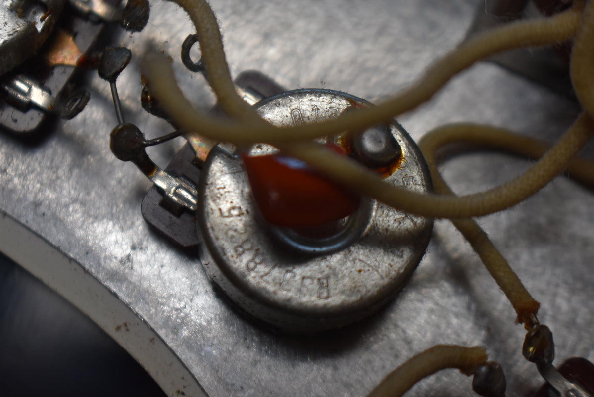 Extreme close-up of a potentiometer with a red capacitor and cream-colored cloth wiring, showing wear and oxidation.