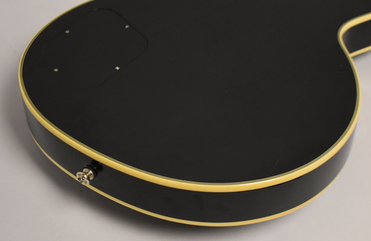 The guitar's black back and sides are visible, with cream binding and a chrome output jack. A control cavity cover is also visible.