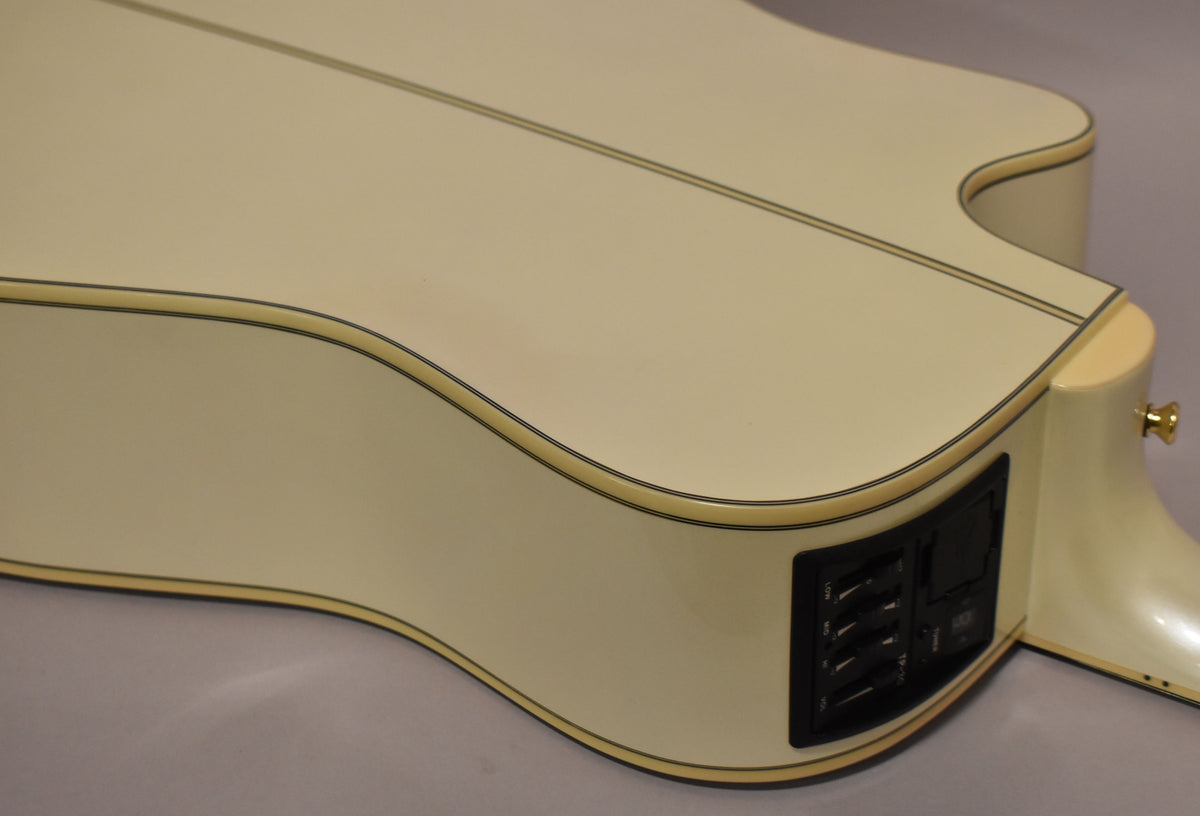 The upper bout of a pearl white acoustic-electric guitar, showing the cutaway, binding, and black preamp controls on the side.