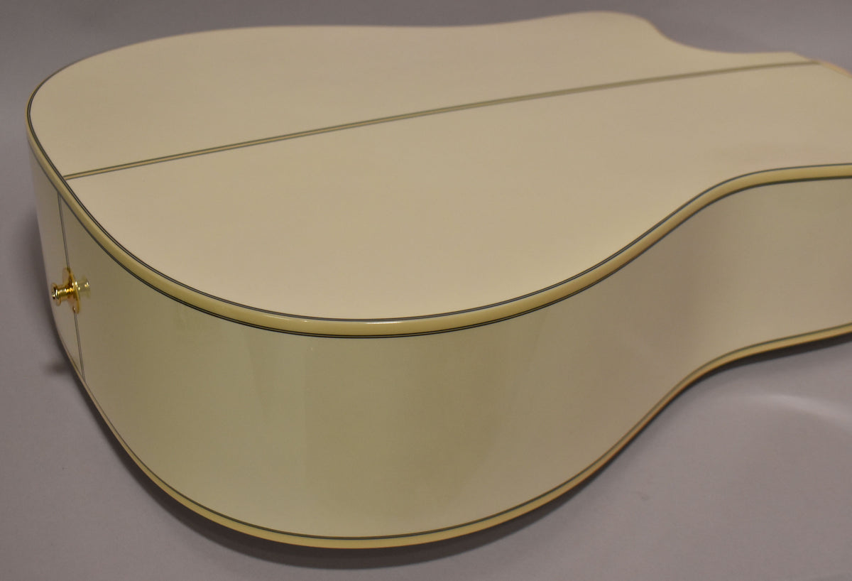 The lower bout of a pearl white acoustic guitar, showing the glossy finish, cream binding, and a gold strap button.