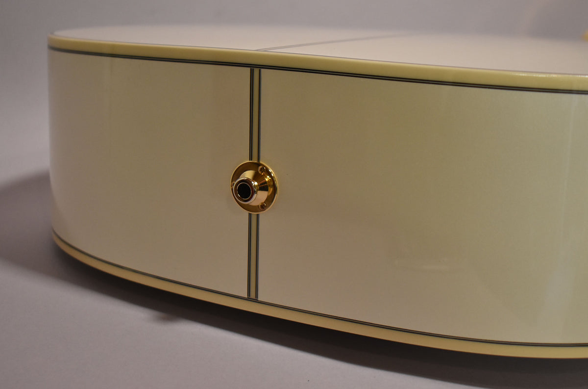 The lower bout of a pearl white acoustic guitar, showing the gold output jack and binding, with faint surface scratches.