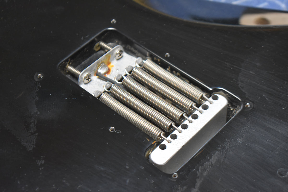 Close-up of the guitar's black body, showing the tremolo spring cavity with five springs and some rust on the tremolo claw.