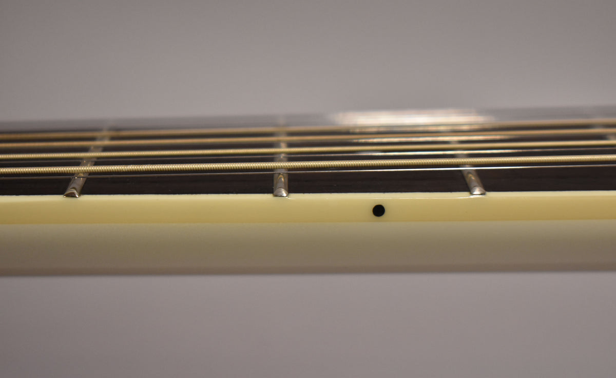 Close-up of the guitar's fretboard from the side, showing the dark fretboard, light strings, and a black side dot marker.