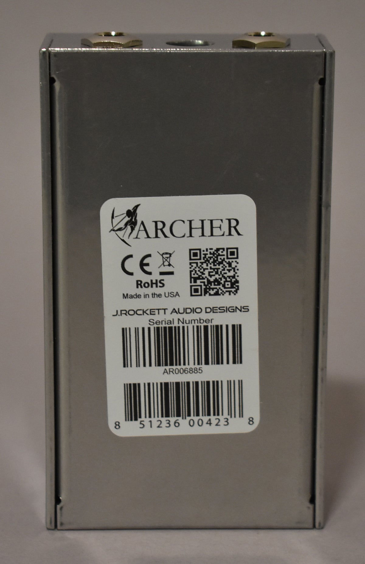 The pedal's silver metal casing is shown from the back, with a large white serial number sticker covering most of the surface.
