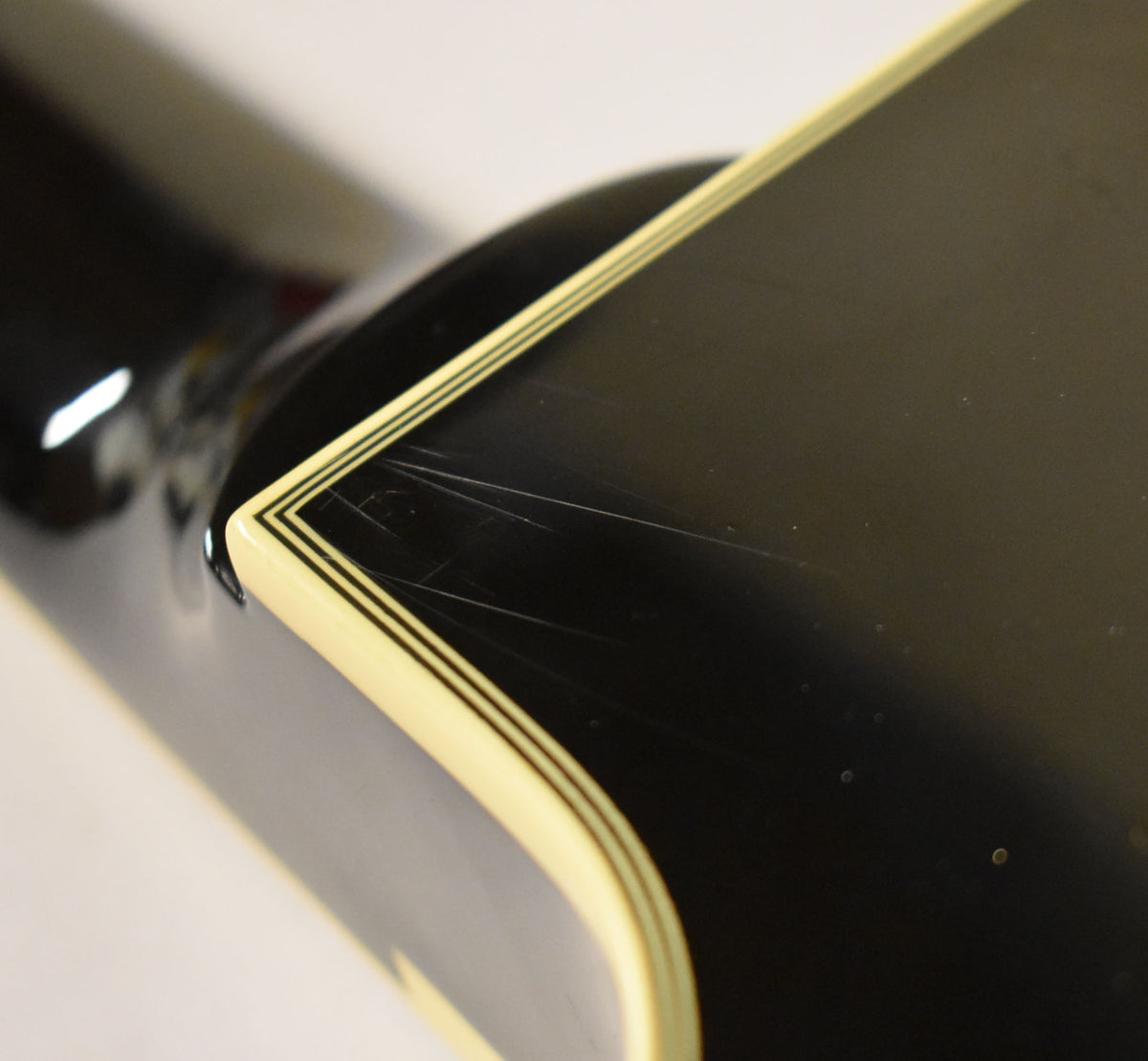 Close-up of the guitar's black body with cream binding and black pinstripes, showing light scratches near the neck joint.