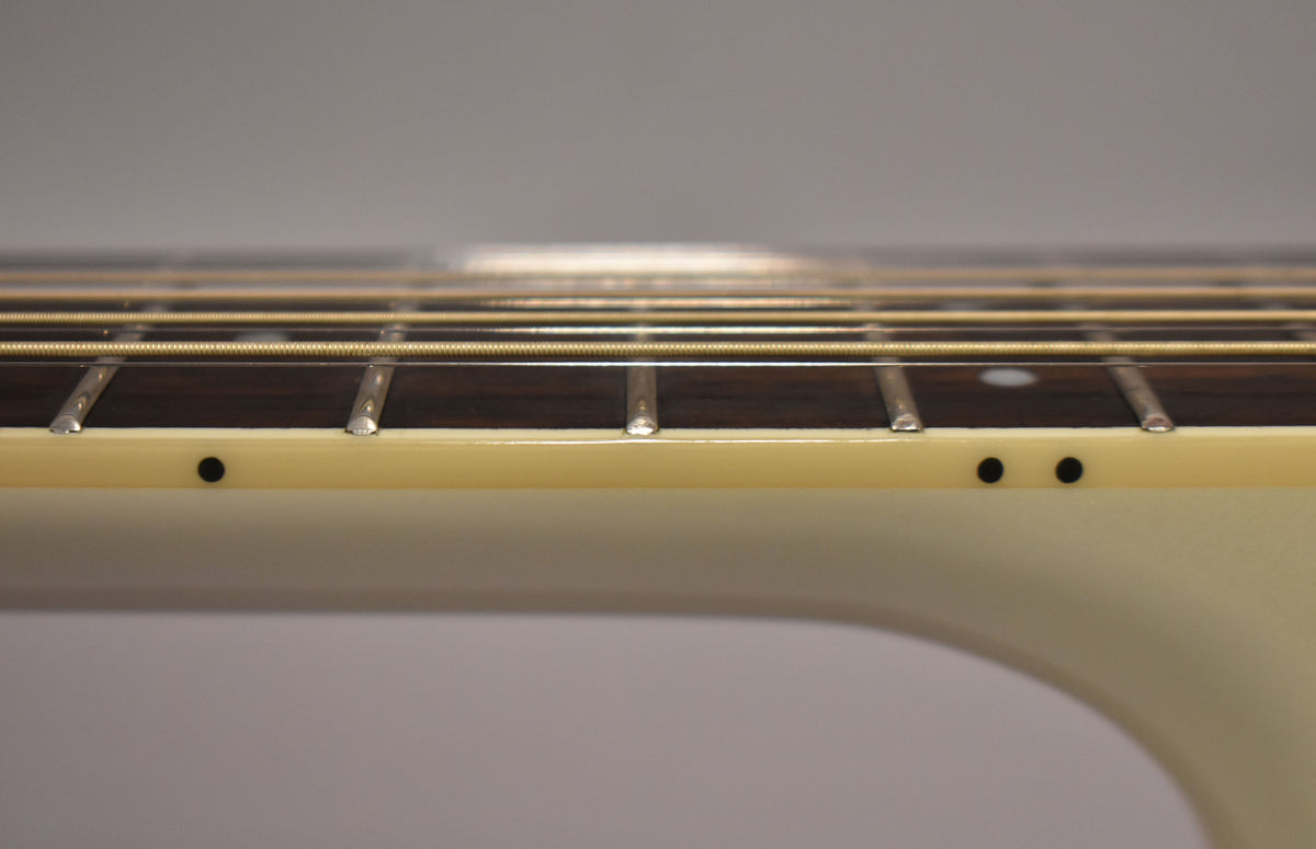 Close-up of the guitar's fretboard and strings from the side, showing dark fret markers on the cream binding and light fret wear.