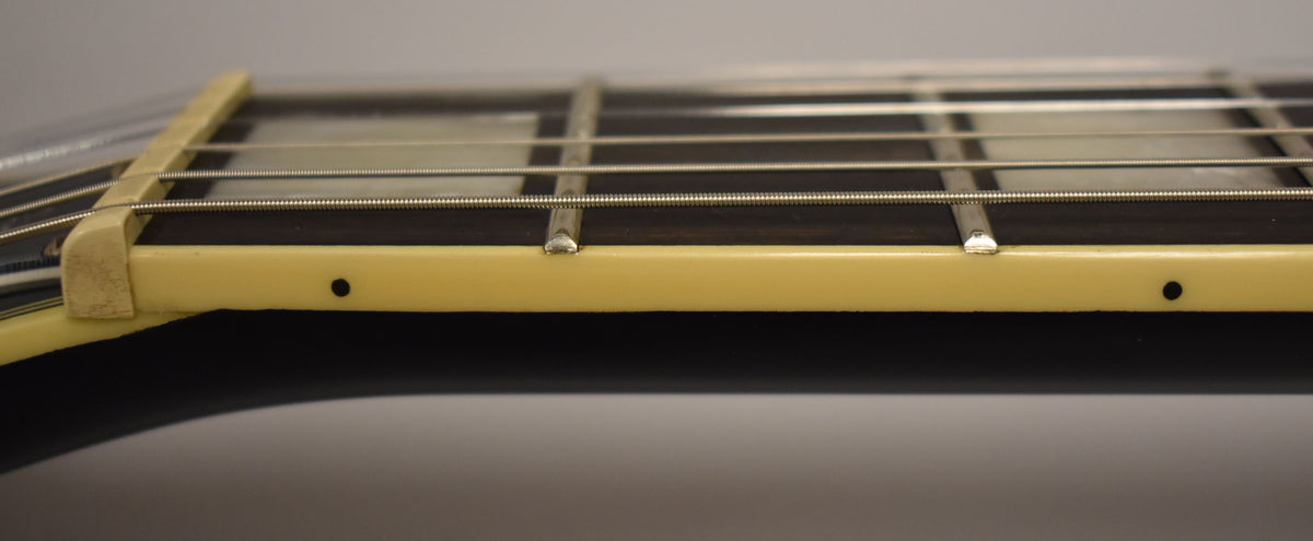 Close-up of the guitar's fretboard from the side, showing the cream binding, dark fretboard, frets, and string nut.