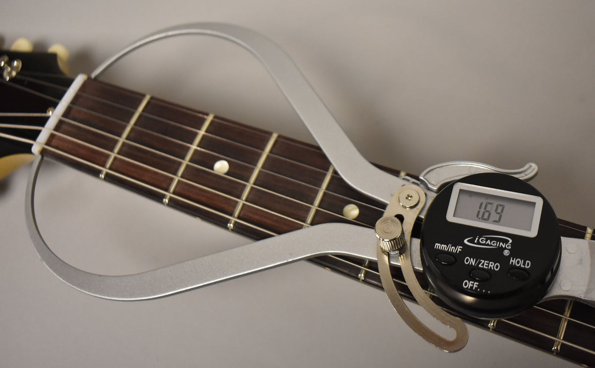 A digital caliper measures the nut width at 1.69 inches, clamped over the dark rosewood fretboard with dot inlays.