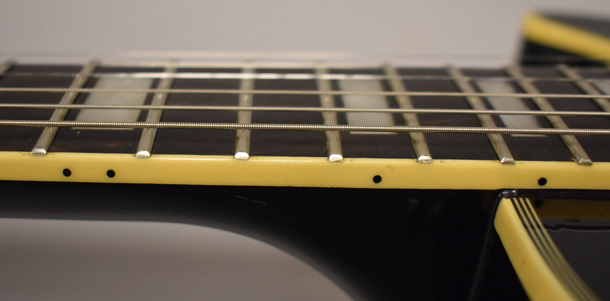 Close-up of the guitar's dark fretboard with block inlays, showing cream binding with black side dots and a small scratch on the body.
