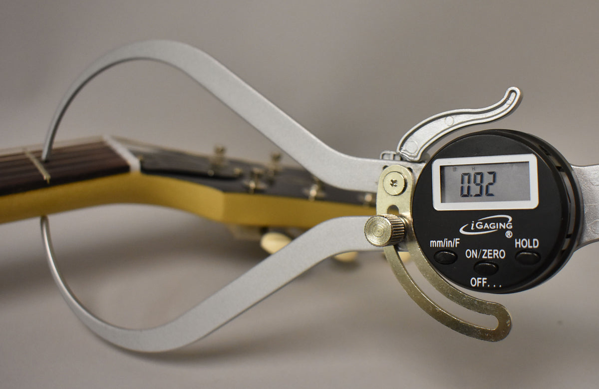 A digital caliper measures the guitar's neck thickness at the first fret, displaying "0.92" on its screen.