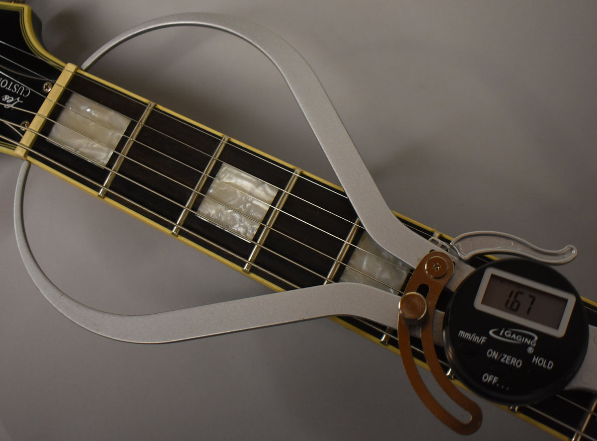 Close-up of the dark fretboard with rectangular mother-of-pearl inlays, showing a digital fret rocker measuring fret height.