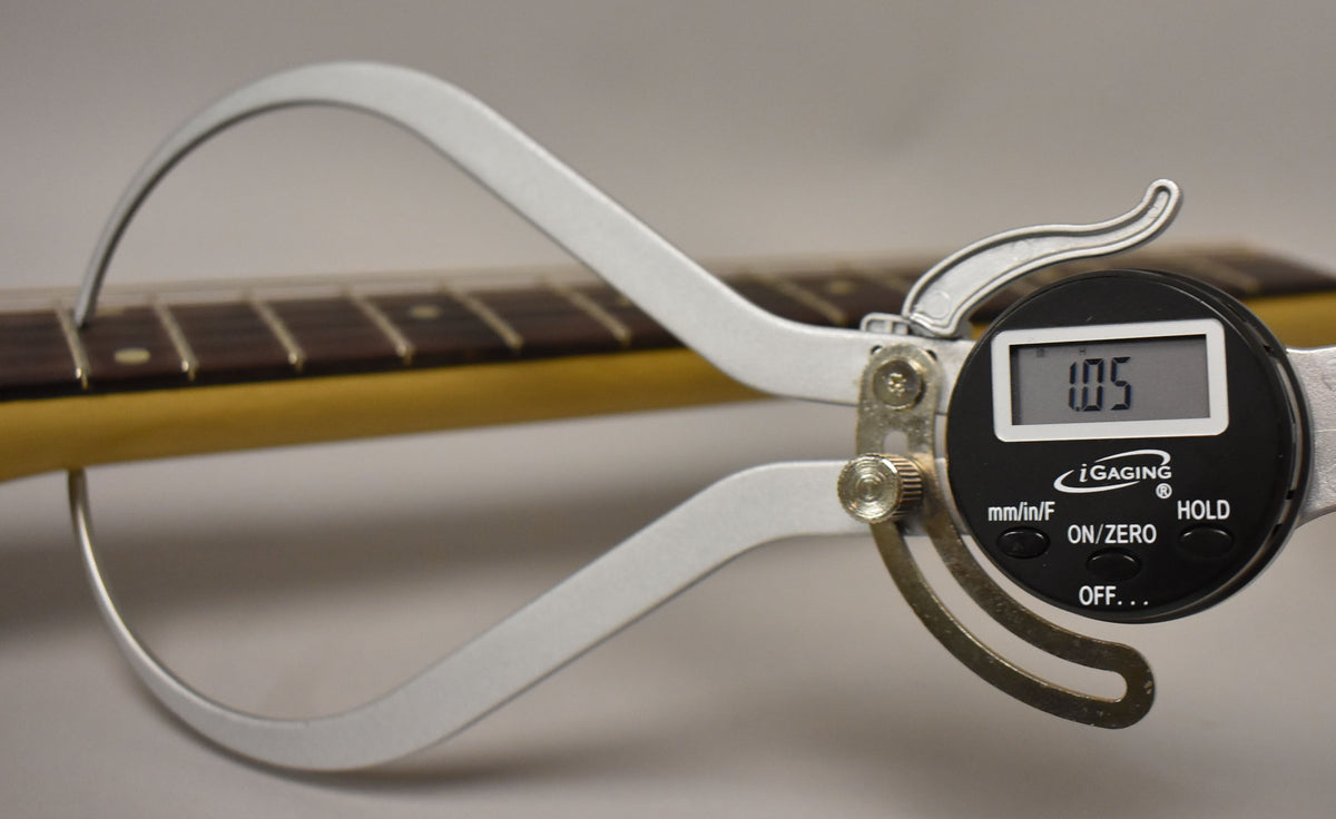 A digital caliper measures the guitar's neck thickness at the first fret, showing 1.05 inches, with a dark rosewood fretboard visible.