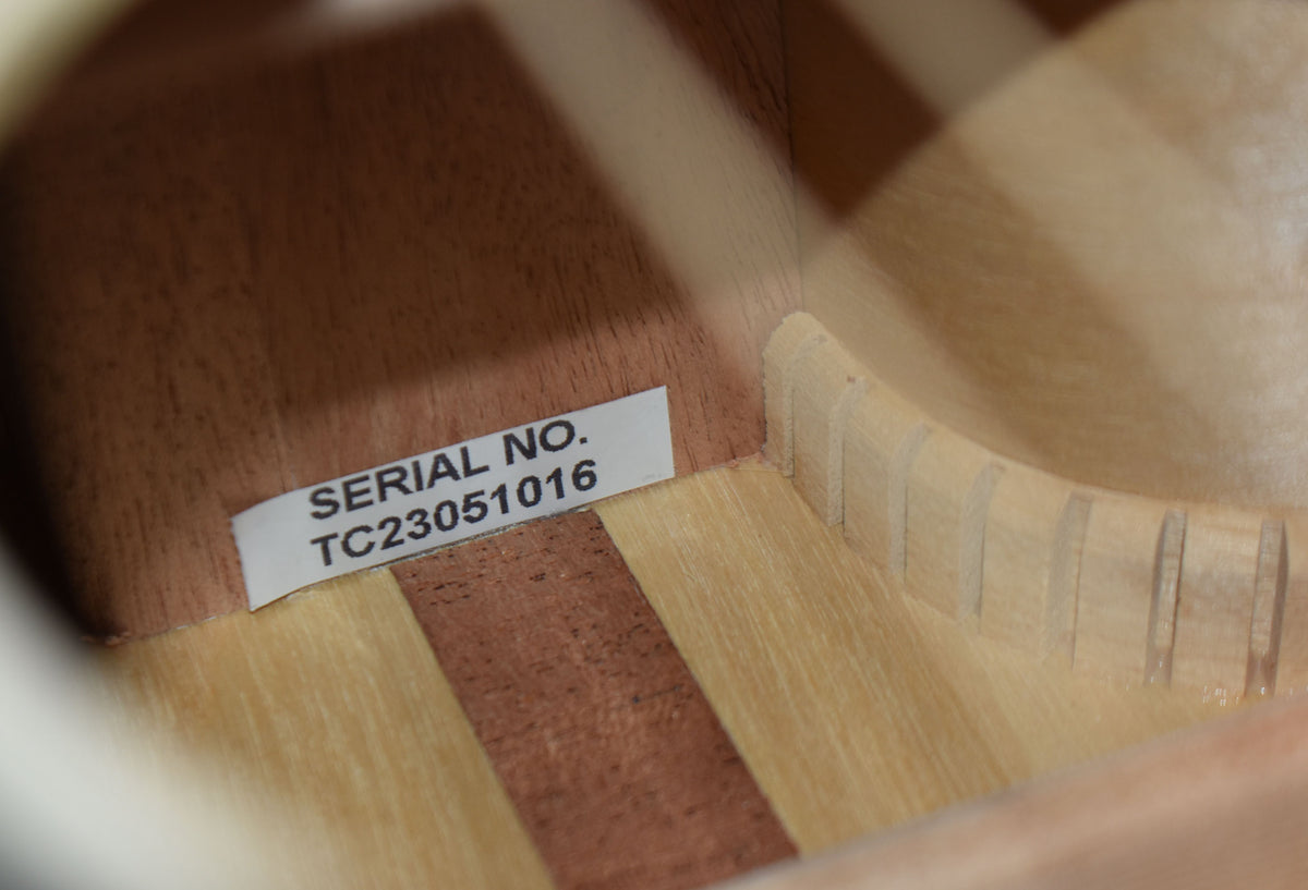 A close-up of the guitar's interior, showing a white serial number sticker on the dark wood back and light wood sides with kerfing.