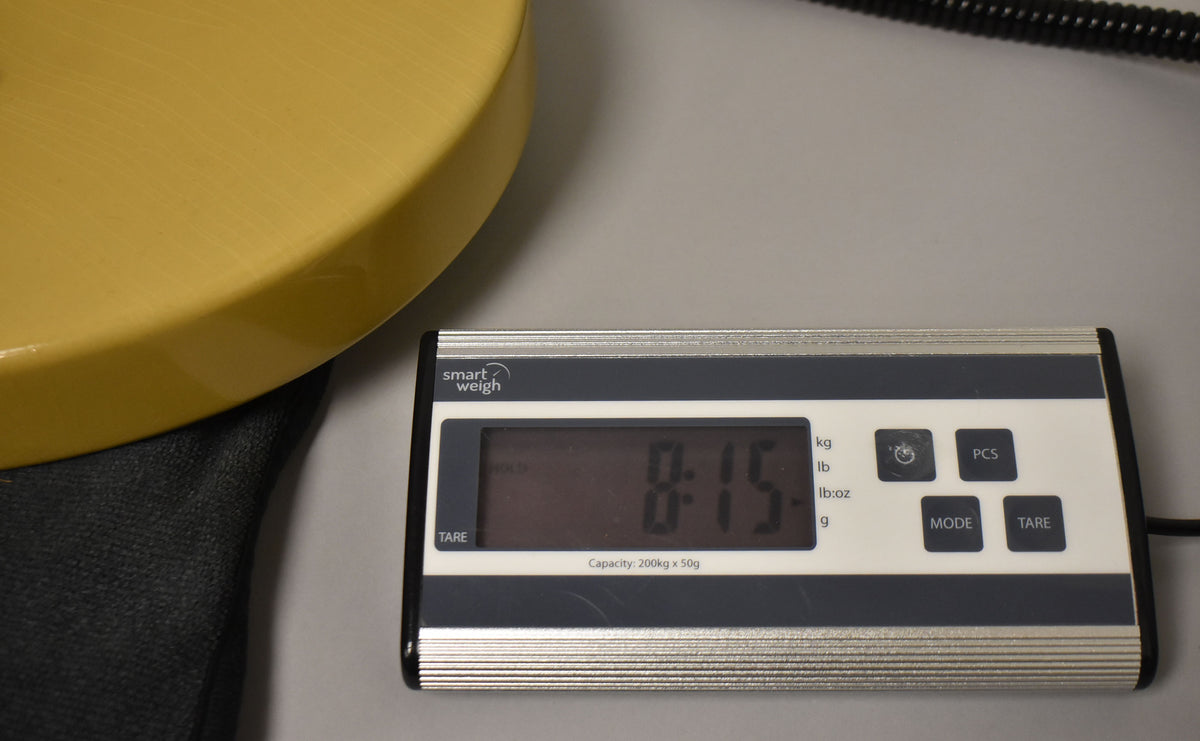 The TV Yellow guitar body rests on a black case, with a digital scale displaying "8.15" in pounds and ounces.