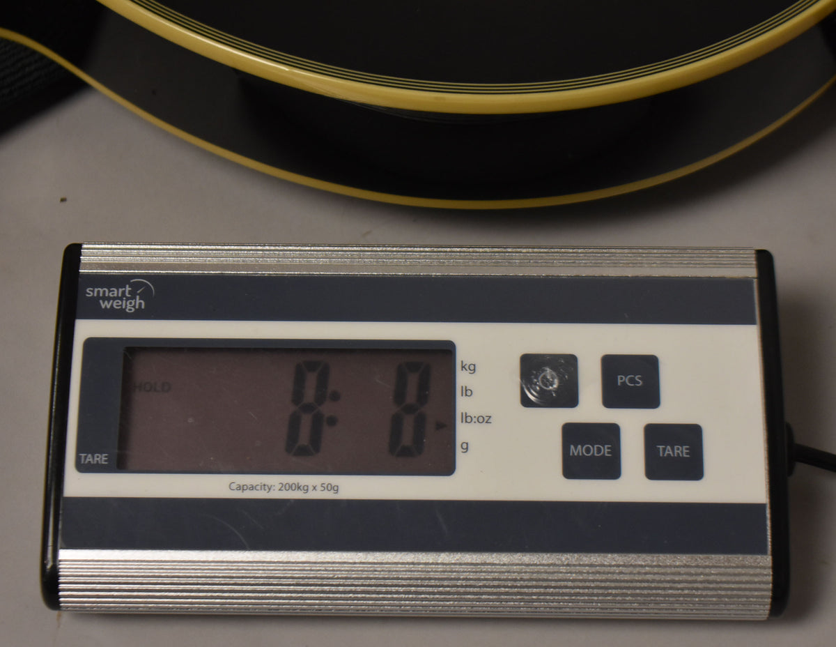 A close-up of a digital scale showing "0.0" with a black guitar body and cream binding visible at the top.