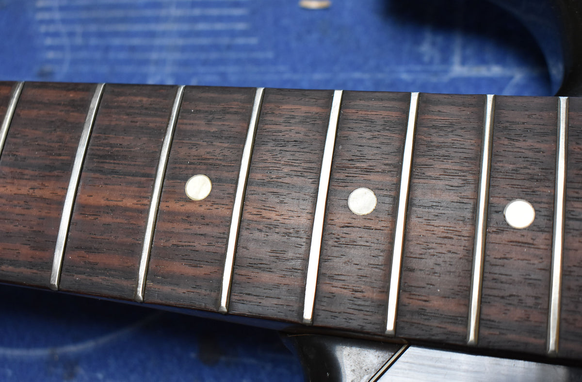 Close-up of the dark rosewood fretboard with light circular inlays and silver frets, showing some wear on the frets.