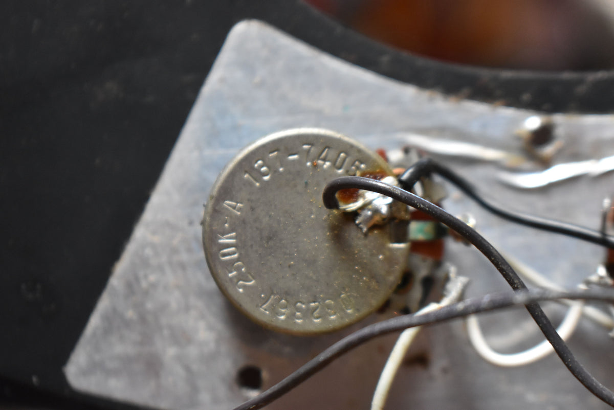Close-up of the bass's internal electronics, showing a metal potentiometer with visible numbers and wires soldered to its terminals.