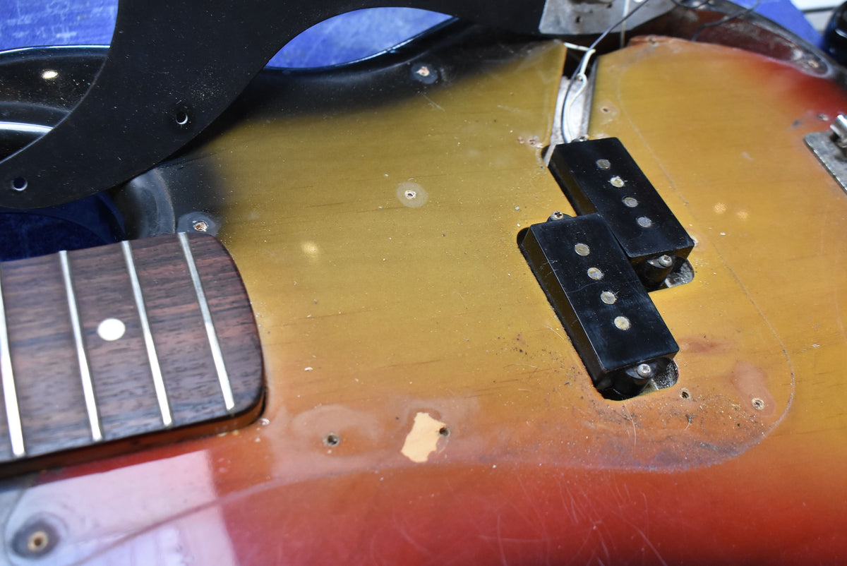 Close-up of the sunburst bass body with the pickguard removed, showing exposed split pickups, wiring, and significant finish wear.