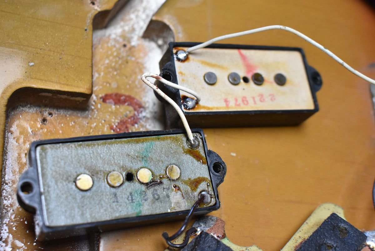 Close-up of two split-coil pickups with exposed pole pieces and wiring, showing wear and a date stamp on the upper pickup.