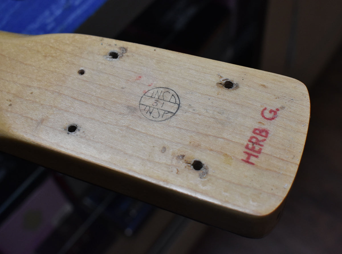 Close-up of the bass neck heel, showing four screw holes, a circular stamp, and "HERB G." written in red.
