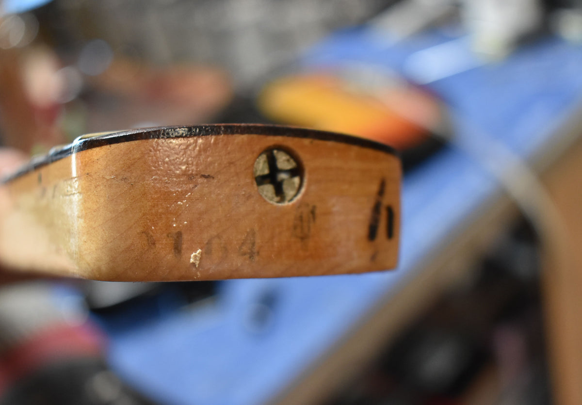 Close-up of the bass neck heel, showing the wood grain, a large Phillips head screw, and some wear and markings.