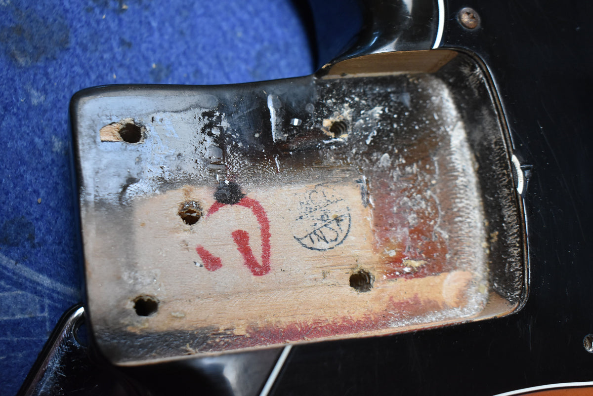 Close-up of the neck pocket, showing exposed wood, black finish chipping, four screw holes, and red and black stamps.