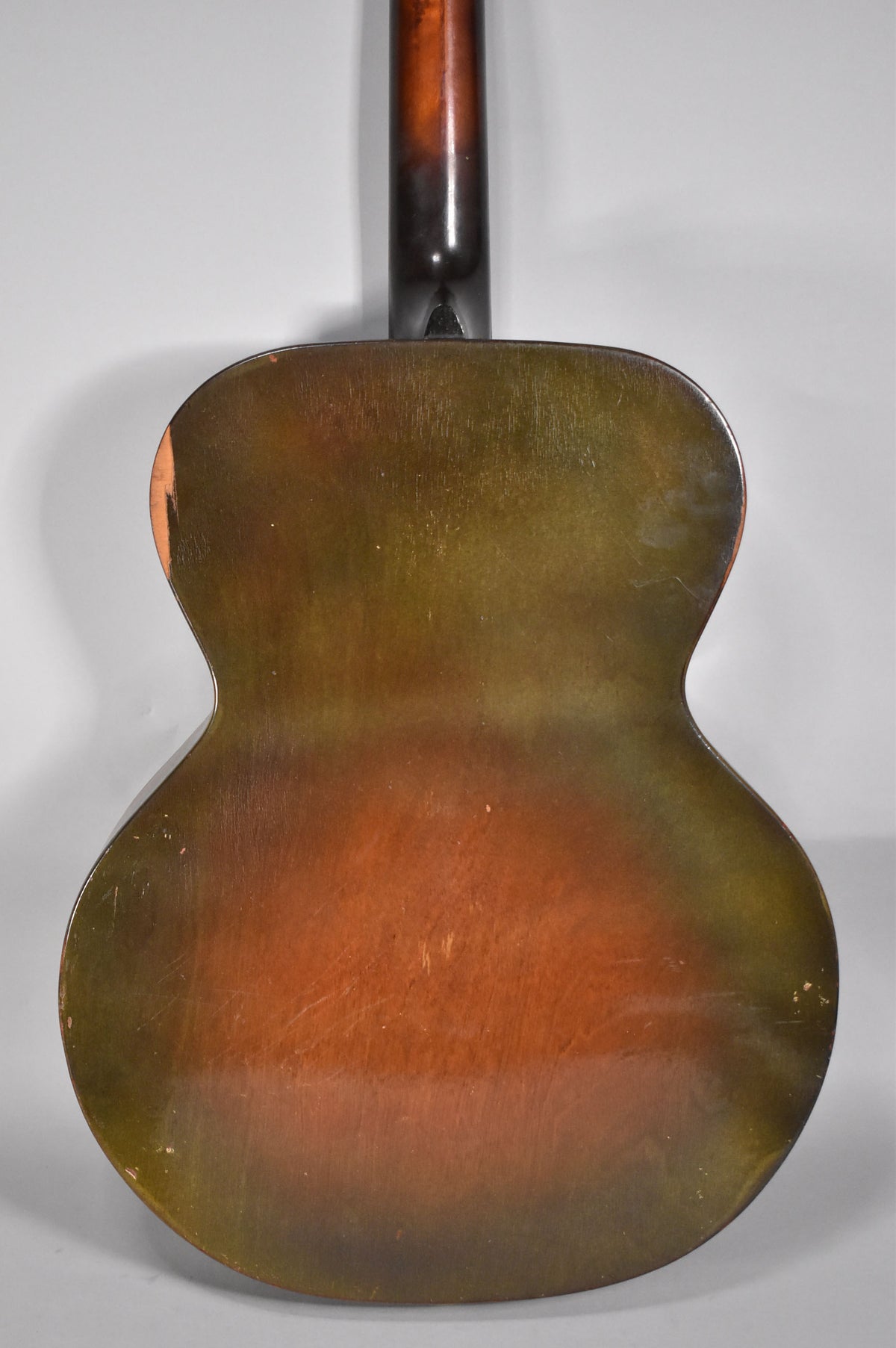 The guitar's back, a dark sunburst with green and brown tones, shows heavy finish wear, scratches, and a chip on the upper left bout.