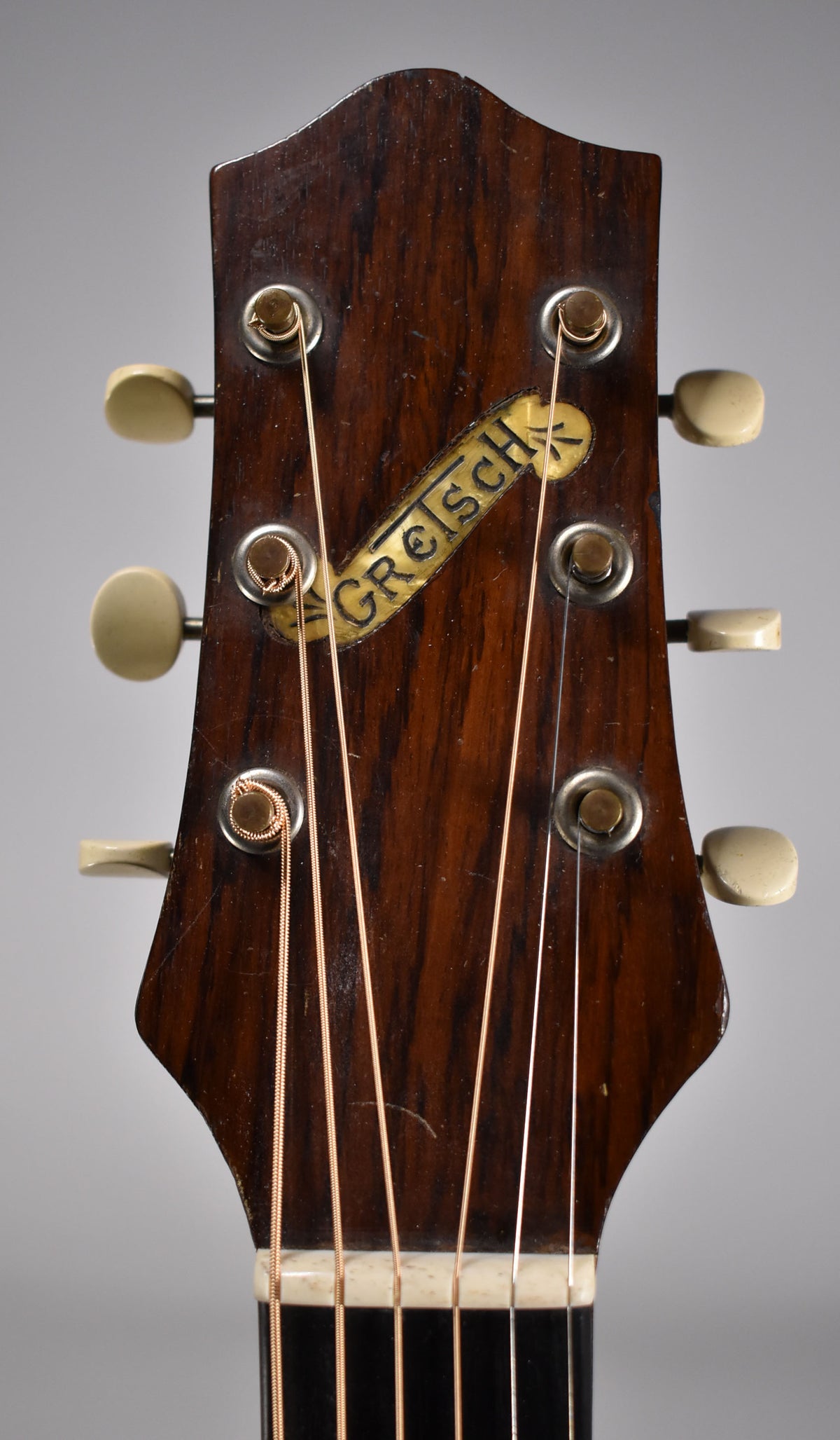 Close-up of the dark brown headstock with a gold and black logo, six cream tuning pegs, and visible wear and scratches.