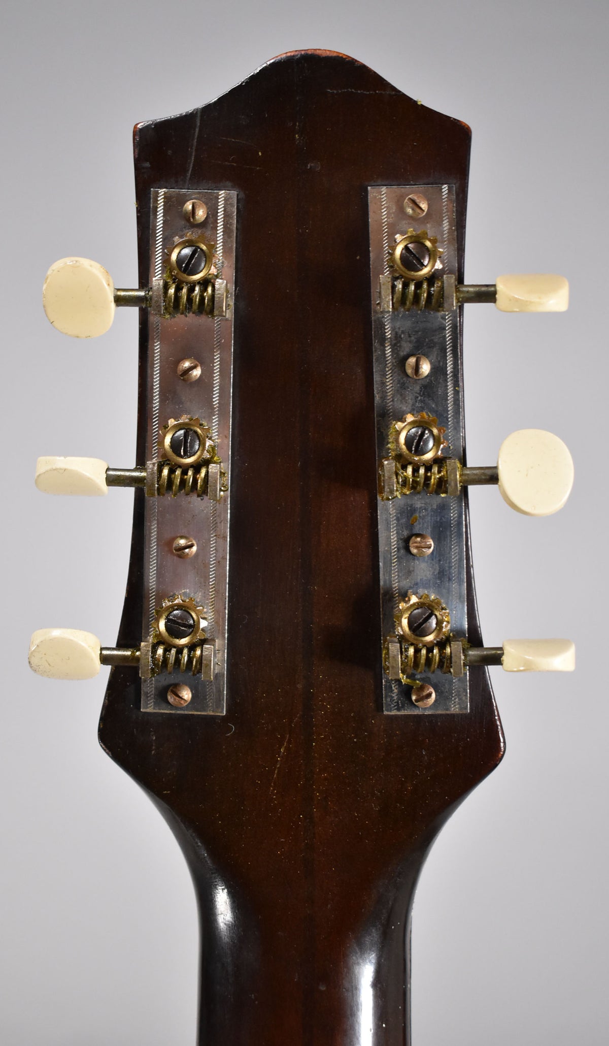 The back of the dark brown headstock and neck, showing six cream tuning pegs on two tarnished metal strips with visible wear.