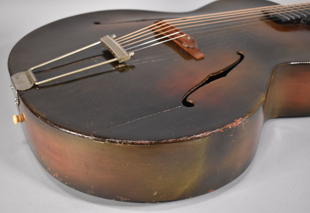 Close-up of the lower bout, showing the dark sunburst finish, f-hole, trapeze tailpiece, and significant finish wear and checking.