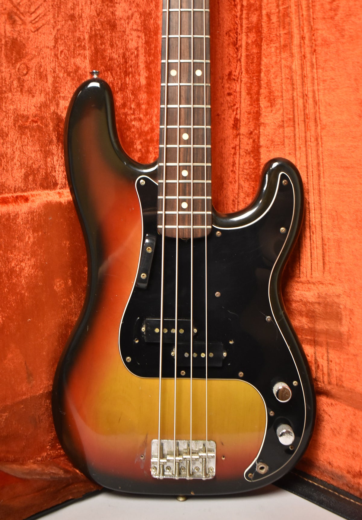 Sunburst bass with a black pickguard, split pickup, chrome bridge, and two control knobs, showing some wear on the body.