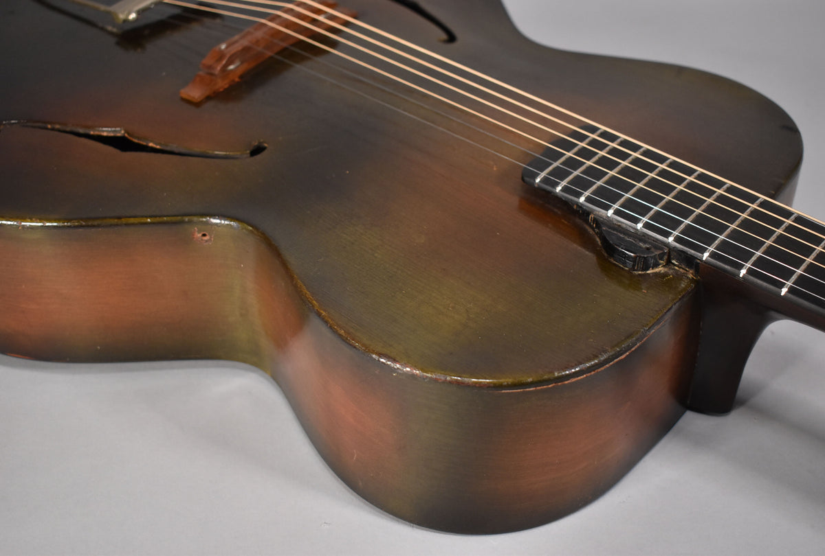 Close-up of the archtop's lower bout, showing the dark sunburst finish, f-hole, and a small hole near the neck joint.