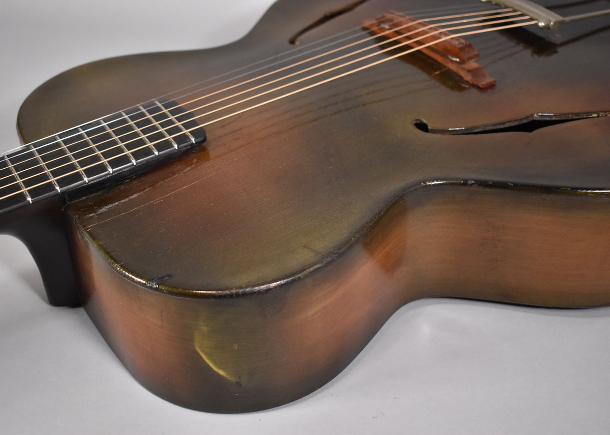 Close-up of the archtop's lower bout and cutaway, showing the dark sunburst finish, f-holes, and a worn wooden bridge.