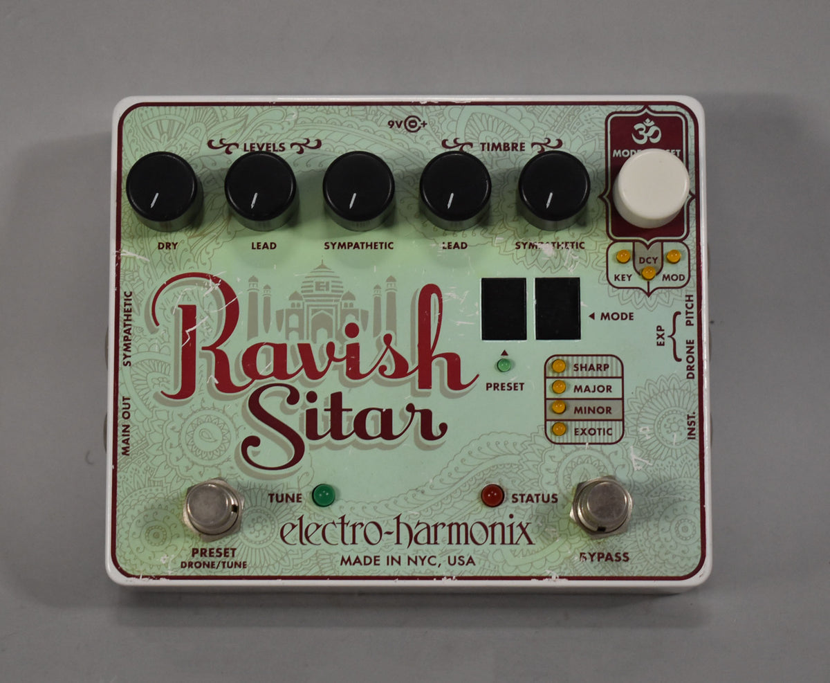 Top-down view of a light green pedal with red lettering, six black knobs, one white knob, and two footswitches.