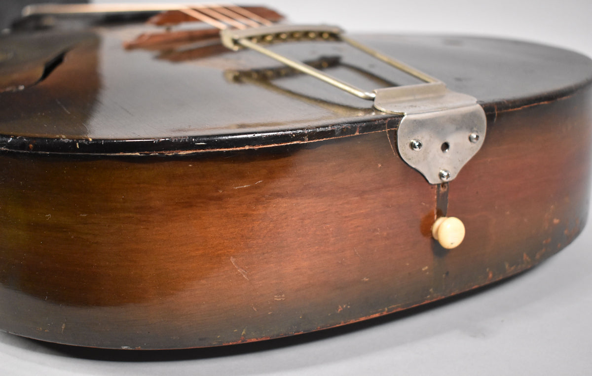 Close-up of the dark sunburst archtop's lower bout, showing a chrome trapeze tailpiece, a cream strap button, and heavy finish wear.
