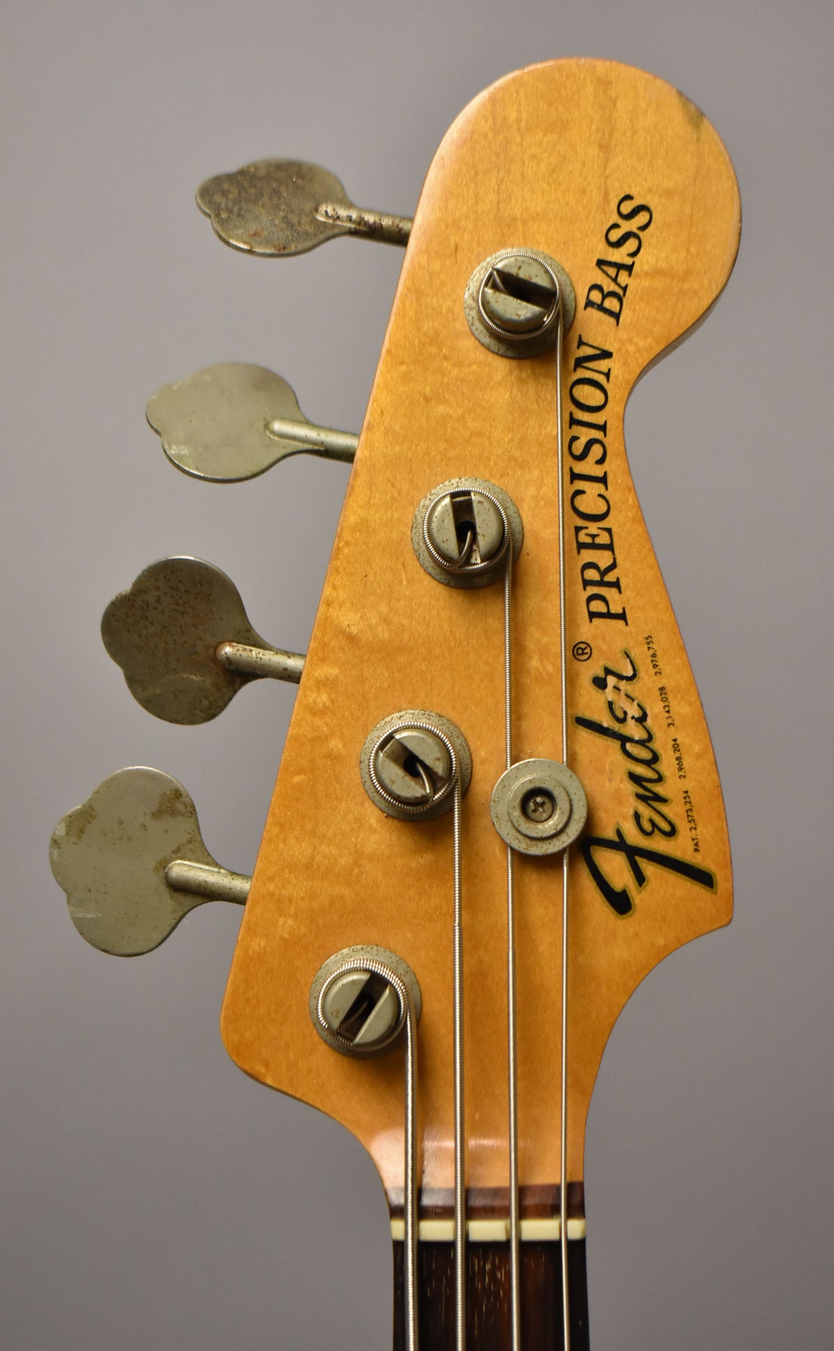 Close-up of the bass headstock, showing the light maple finish, four tarnished clover-leaf tuners, and string tree.