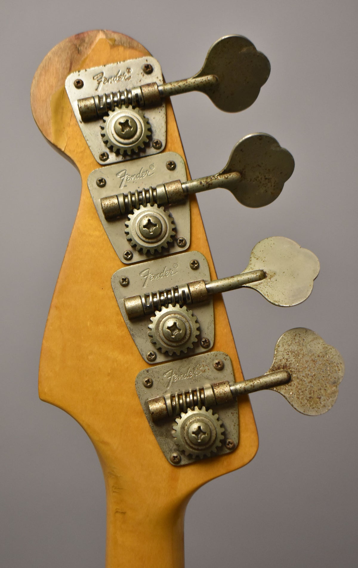 Close-up of the bass headstock from behind, showing four rusty, clover-leaf tuners on a worn maple neck.