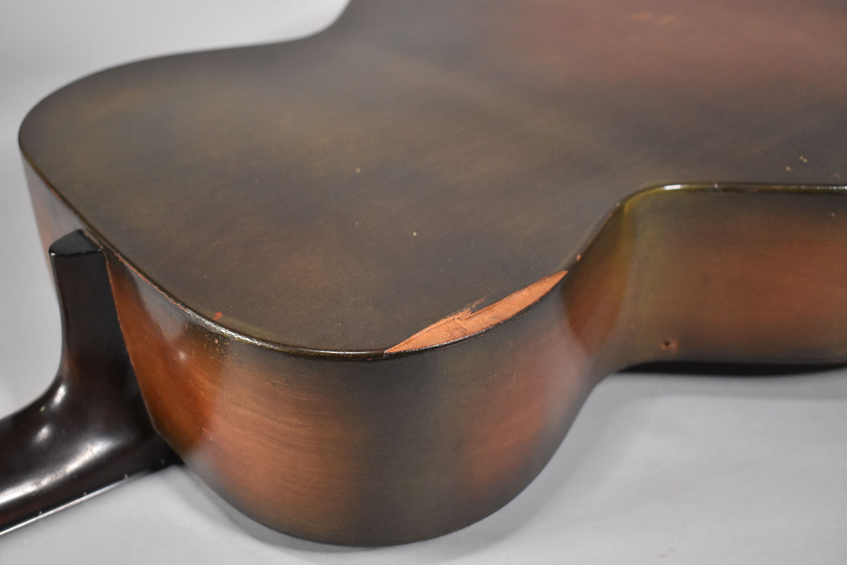 Close-up of the guitar's lower bout and neck heel, showing a dark brown sunburst finish with significant wear and a large chip on the lower edge.
