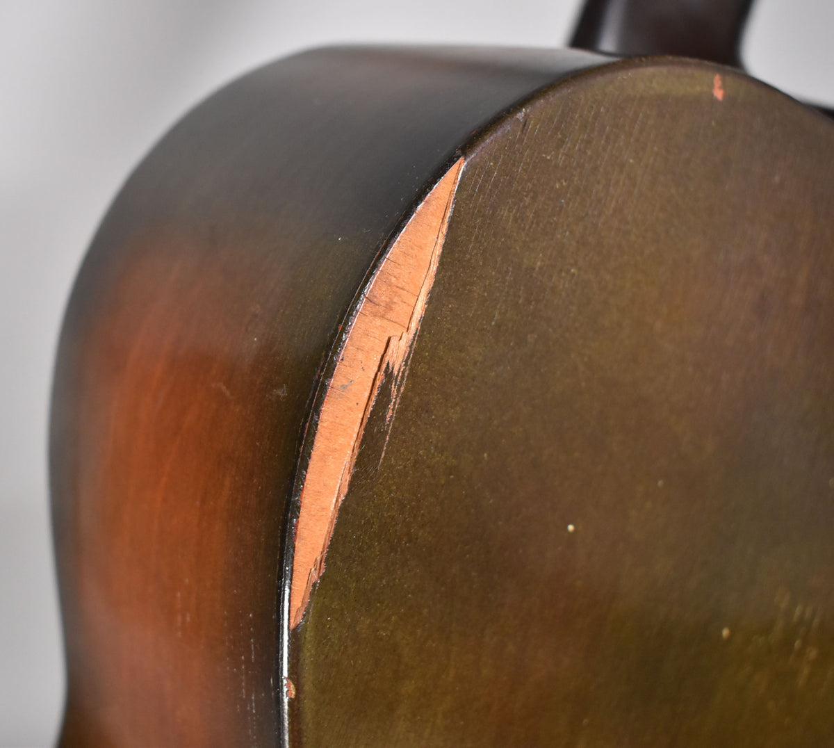 Close-up of the guitar's dark sunburst body, showing a large chip on the lower bout's edge revealing the lighter wood underneath.