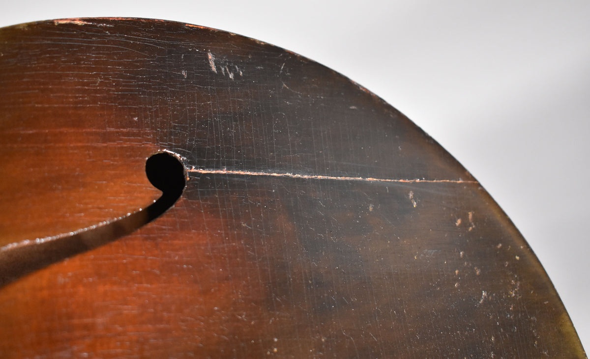 Close-up of the guitar's dark brown sunburst top, showing a f-hole and a long crack running horizontally across the body.